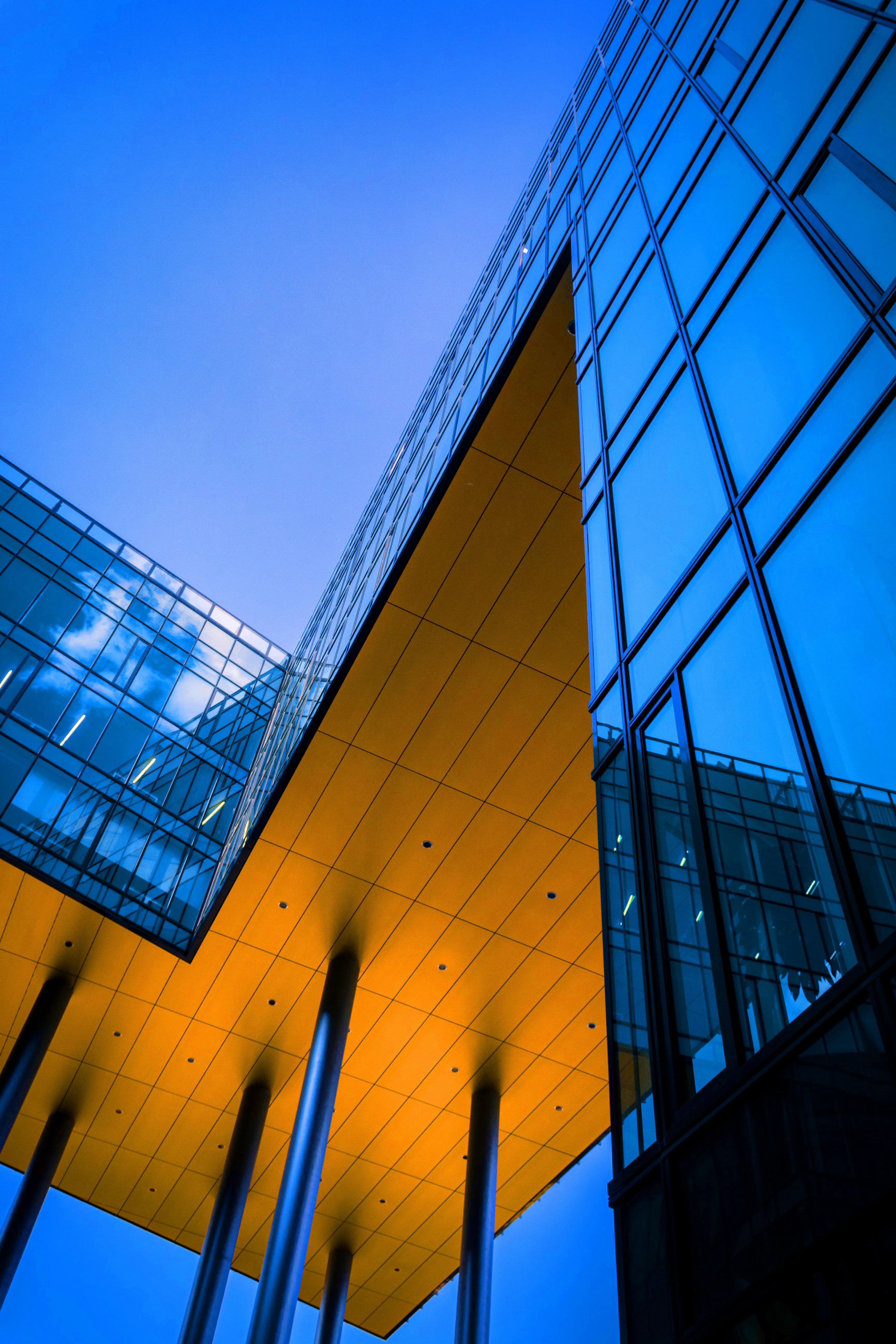 Futuristic architectural exterior featuring glass, metal, and sharp angles. The design is modern and sleek, with blue and orange lighting creating a dramatic effect.