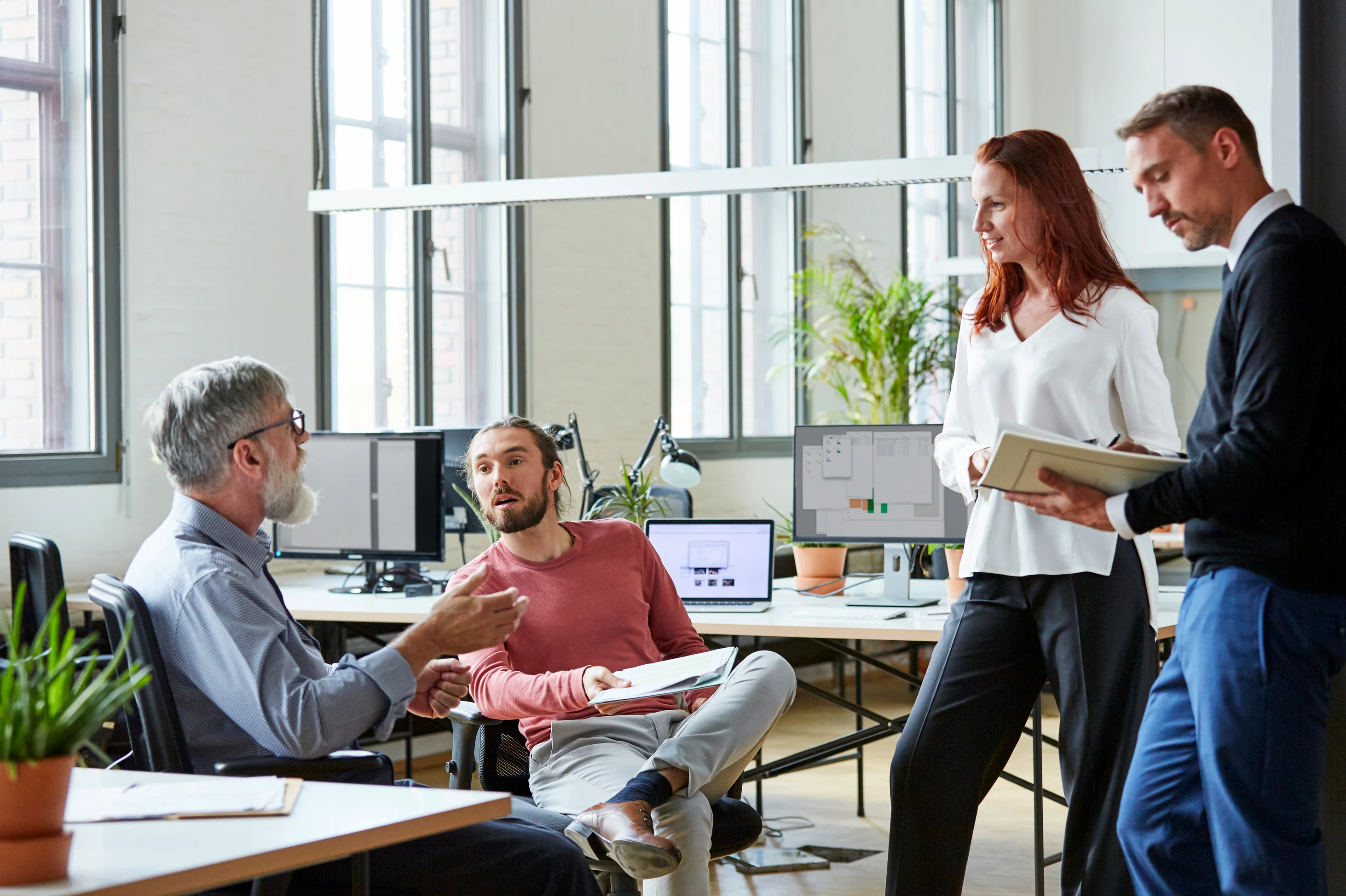 Four professionals in a modern office discussing work.